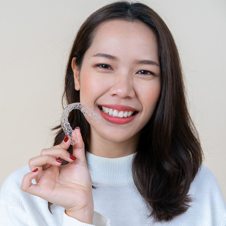 woman smiling while holding Invisalign aligner