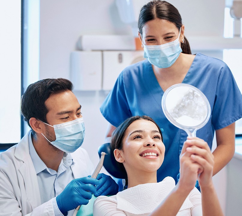 Patient smiling at reflection next to dentist and dental assistant