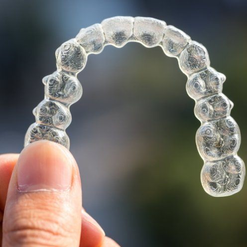 Hand holding Invisalign clear aligner outdoors in sunlight