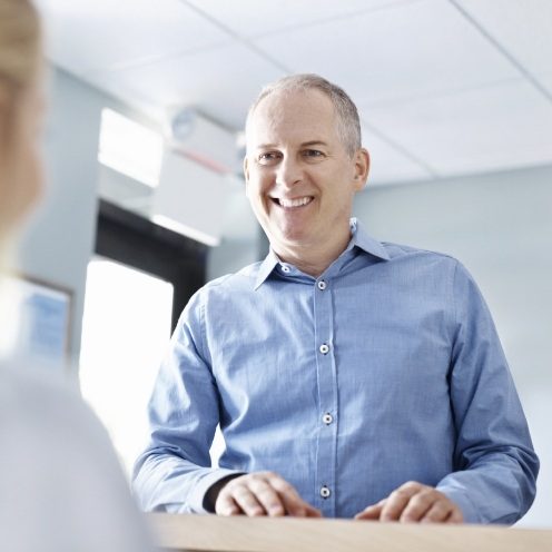 Man in light blue button down shirt talking to dental team member