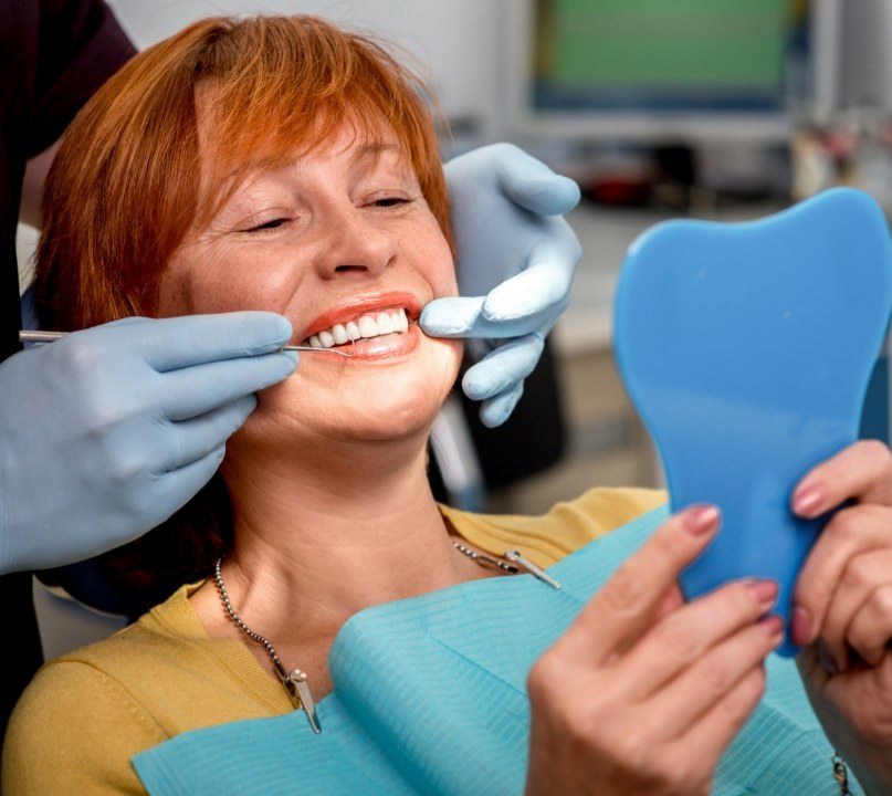 Woman in dental chair admiring her smile after replacing missing teeth