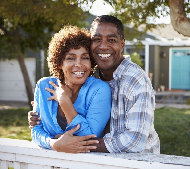 Older man and woman smiling in their front yard after restorative dentistry in Palos Heights