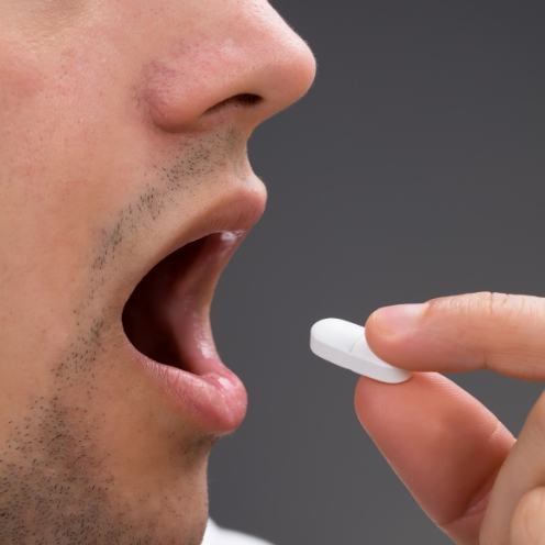 Close up of man placing white pill in his mouth