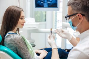 Dentist showing model dental implant to a woman with brown hair